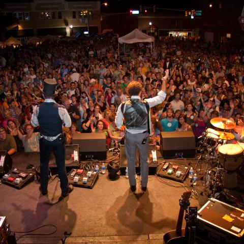 band of four facing large crowd at night. Lead singer with hand up