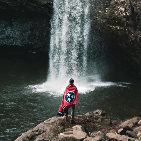 Man standing in front of Foster Falls with Tennessee state flag