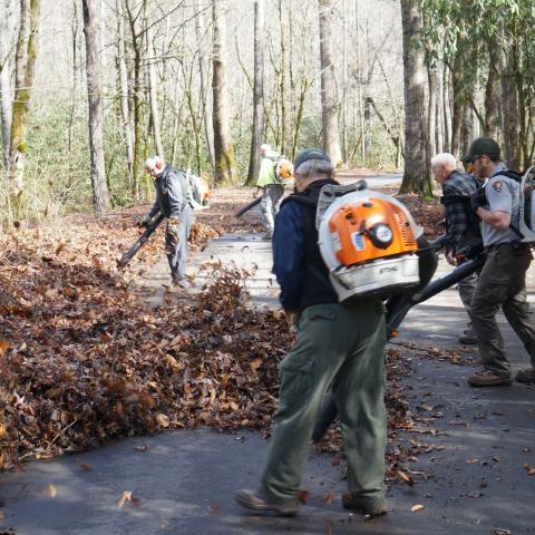 Volunteers and staff members use leaf blowers to remove debris